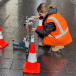 Technician in high-vis vest performing slip test on pavement