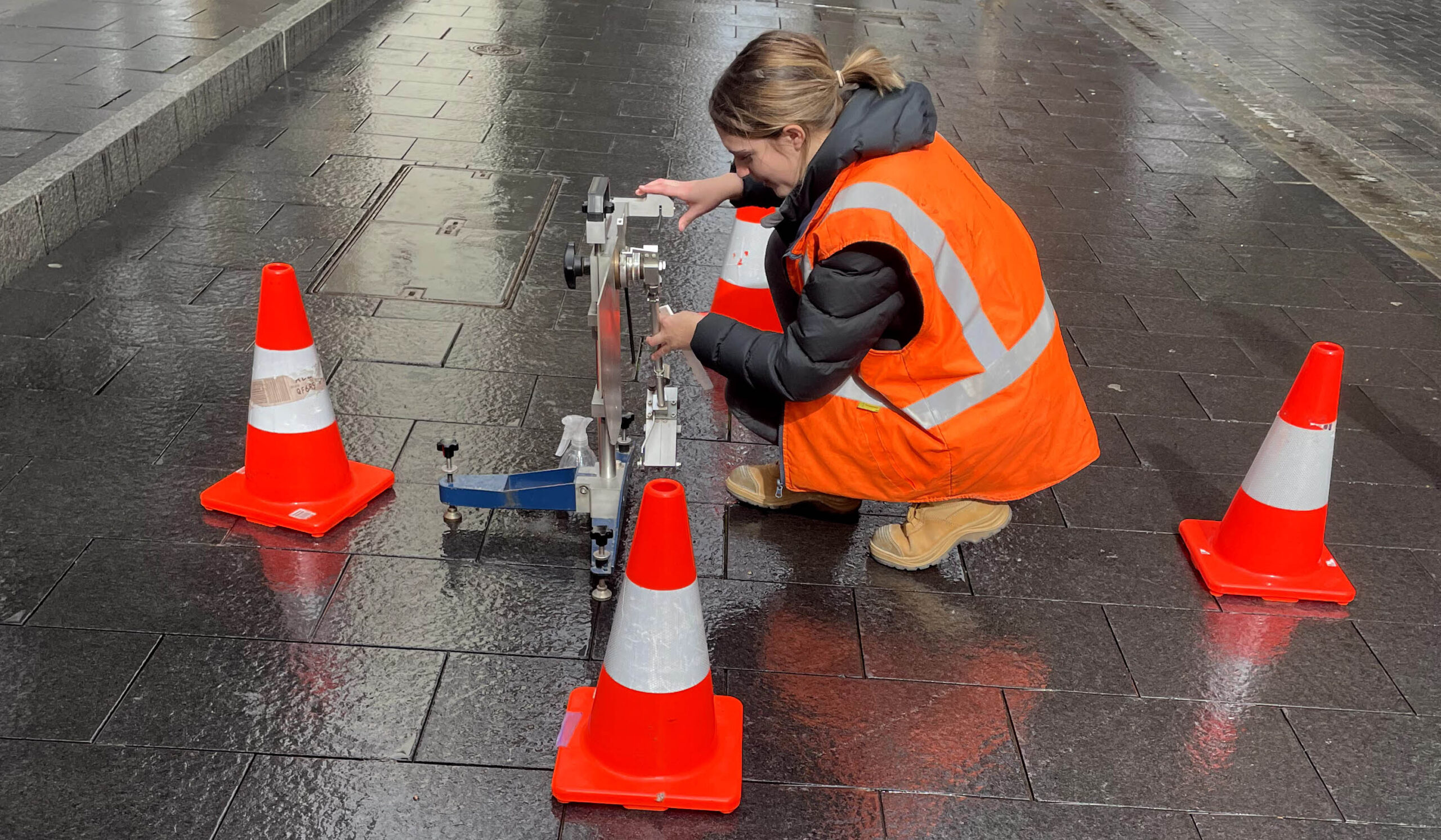 Technician in high-vis vest performing slip test on pavement